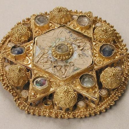 A circular gold brooch set with stones round a central boss.