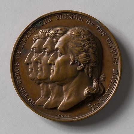 A bronze medal with three portrait heads in profile.
